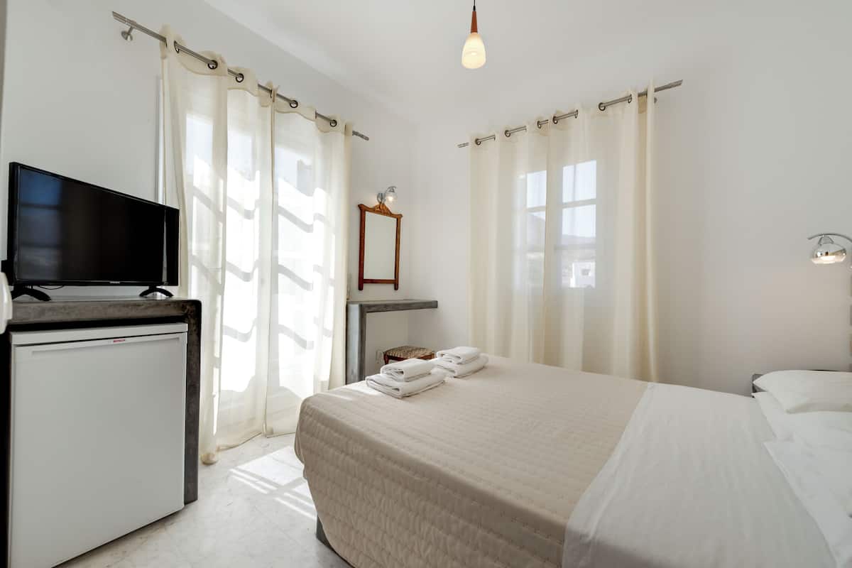 Une chambre d’hôtel avec un lit, un téléviseur posé sur un meuble, une petite table et un miroir.