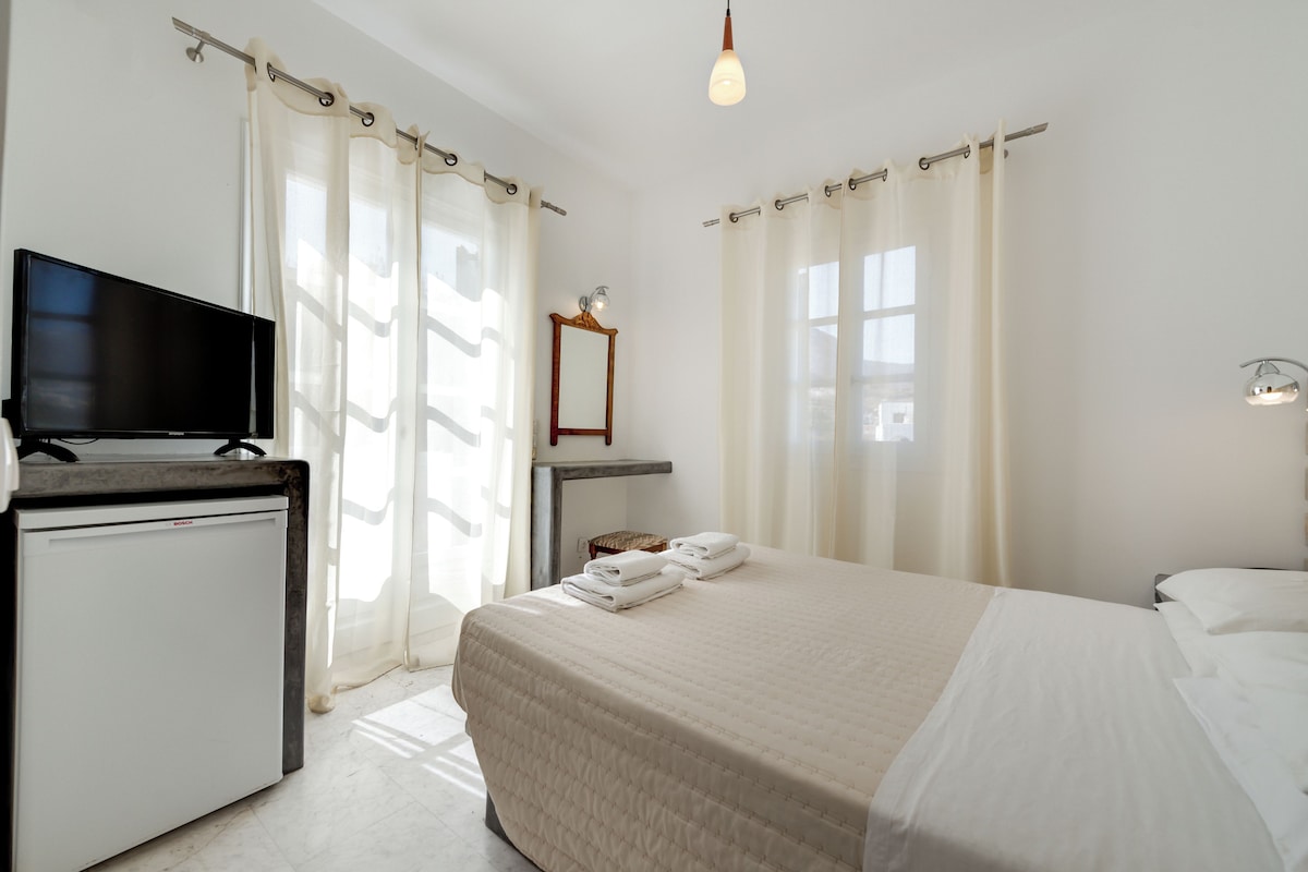 A hotel room with a bed, a television on a stand, a small table, and a mirror.