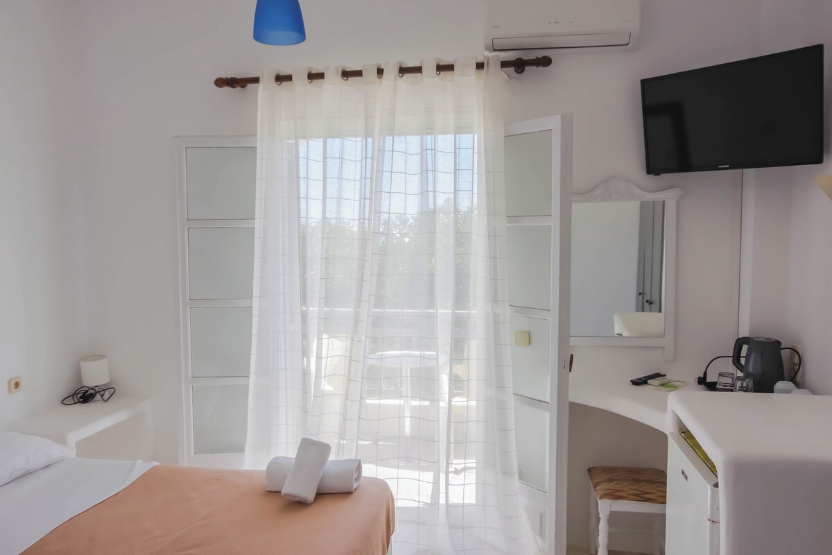 A hotel room with a bed, a desk, a chair, a television, and a window with curtains.