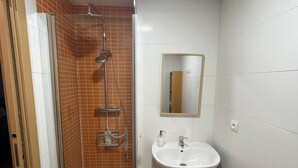 A bathroom with a glass-enclosed shower, a white sink, and a mirror above it.
