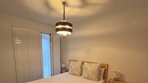 A bedroom with a large bed, a bedside table with a lamp, and a hanging light fixture.