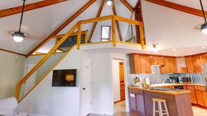 A spacious kitchen with wooden cabinets, a central island, and a staircase leading to an upper level. - Unique Cabin w/ Riverside View + Hot Tub + Apple Pie (Ellijay)