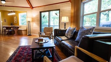 Un salon chaleureux avec un plancher en bois, un canapé en cuir, une table à manger et une grande fenêtre agrémentée de rideaux.