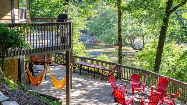 A deck with outdoor furniture, a hammock, and a view of a river surrounded by trees. - Unique Cabin w/ Riverside View + Hot Tub + Apple Pie (Ellijay)