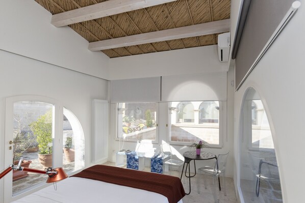 A bright room with a bed, a desk, and large windows.