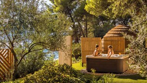 A hot tub surrounded by lush greenery and a wooden fence, with a view of the sea in the background.