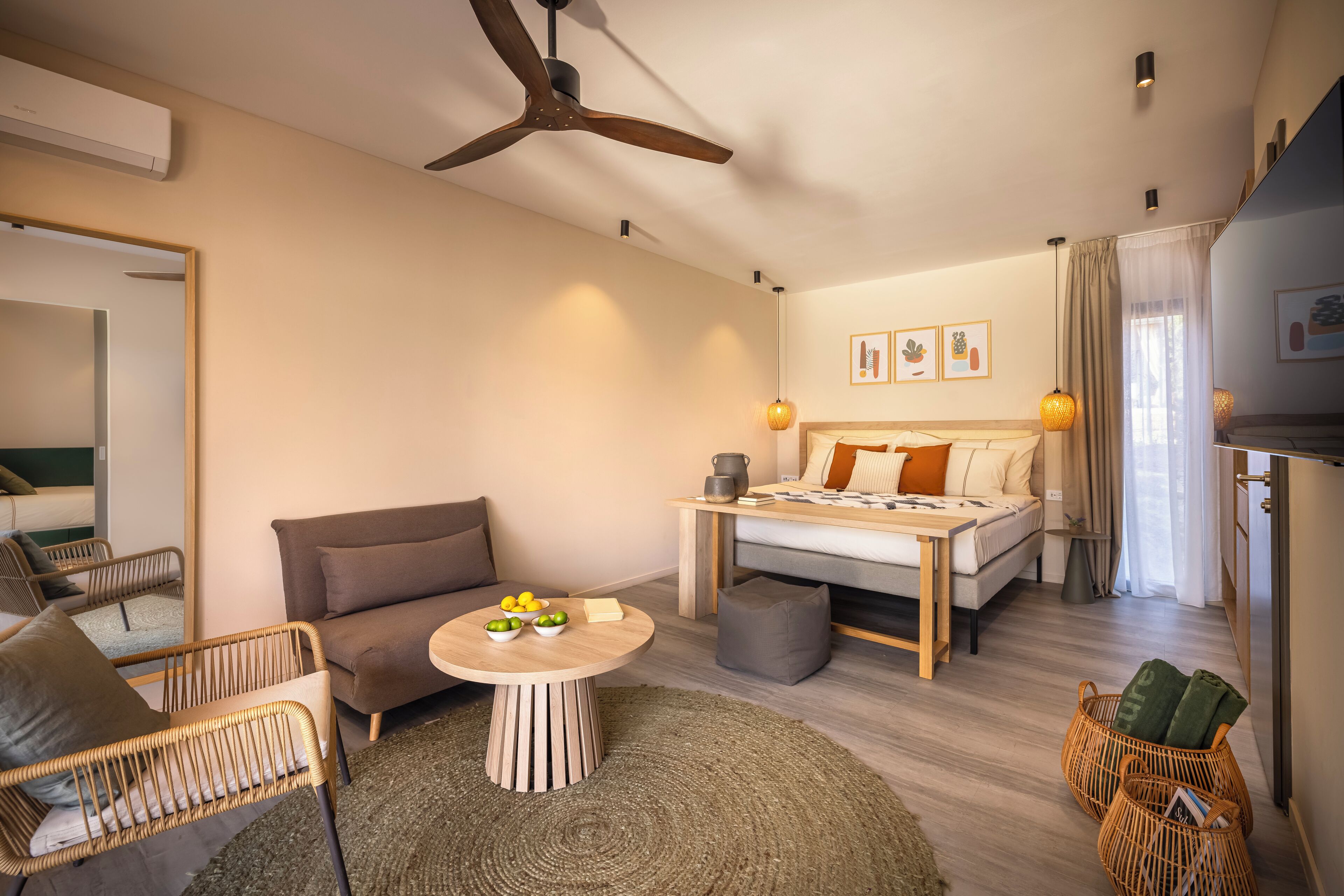 A modern hotel room with a bed, sofa, dining table, and wicker furniture.