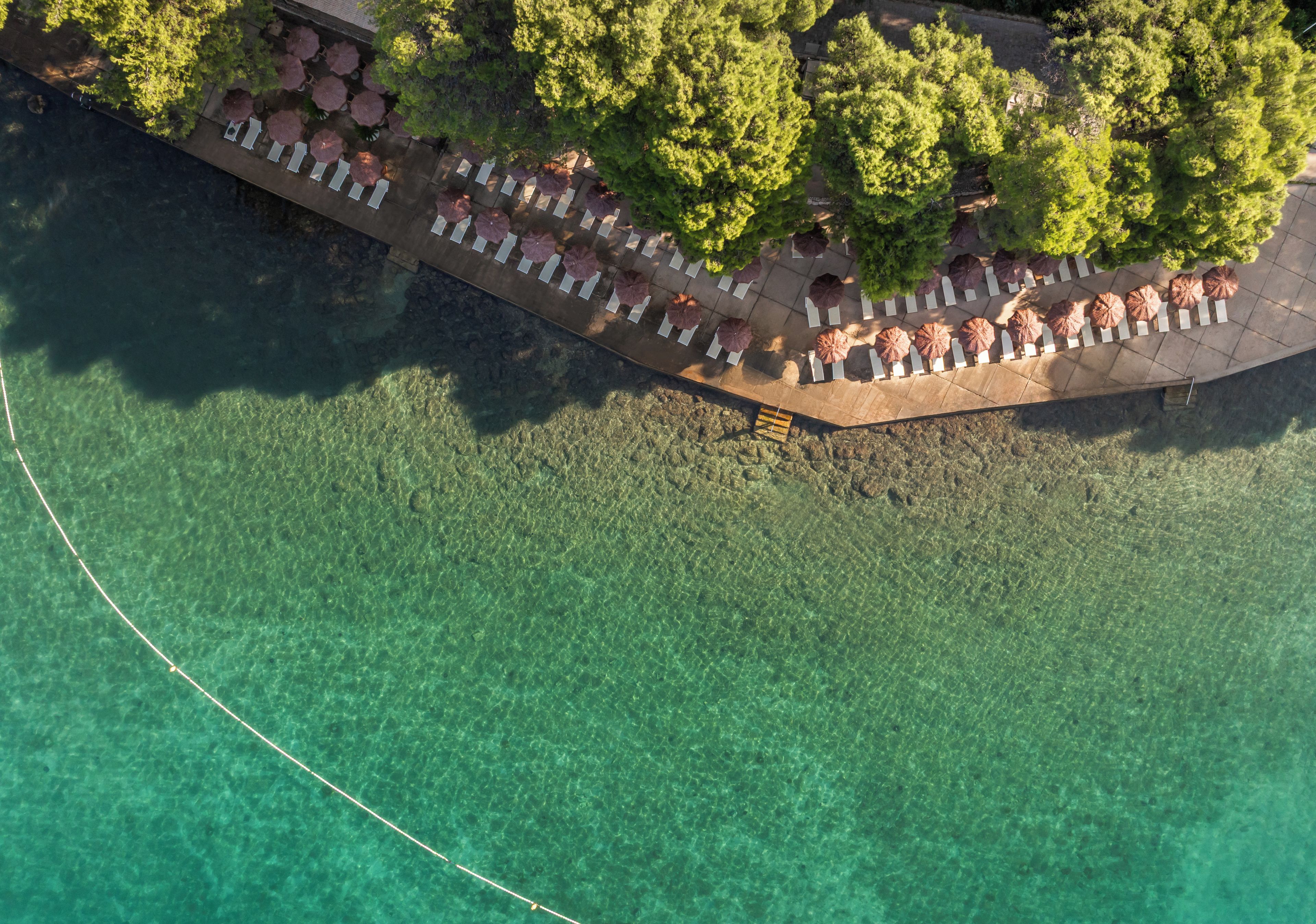 An aerial view of a waterfront property with a patio area, clear water, and surrounding greenery.