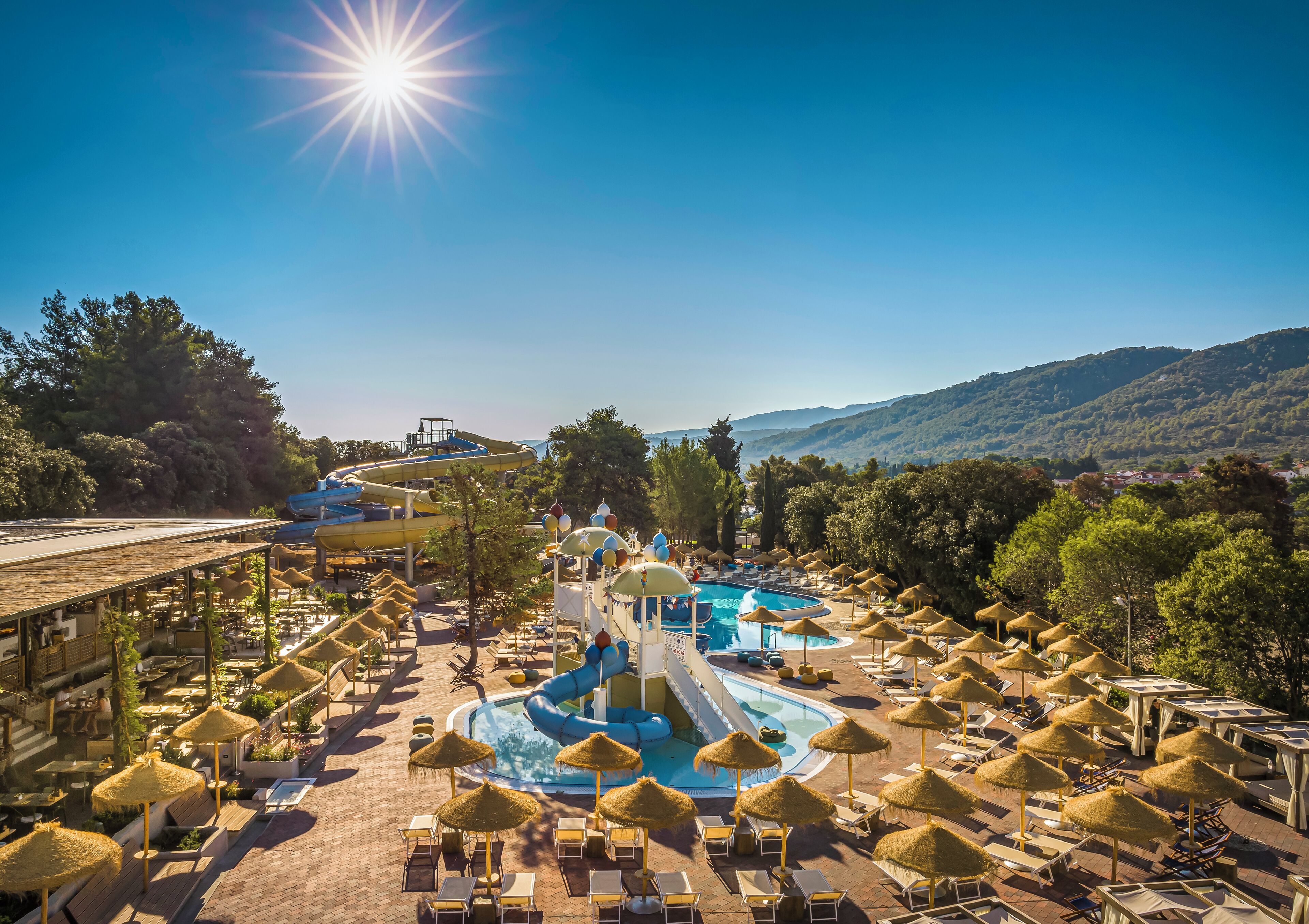 Un resort con piscina, toboganes acuáticos y sillones de descanso bajo sombrillas.