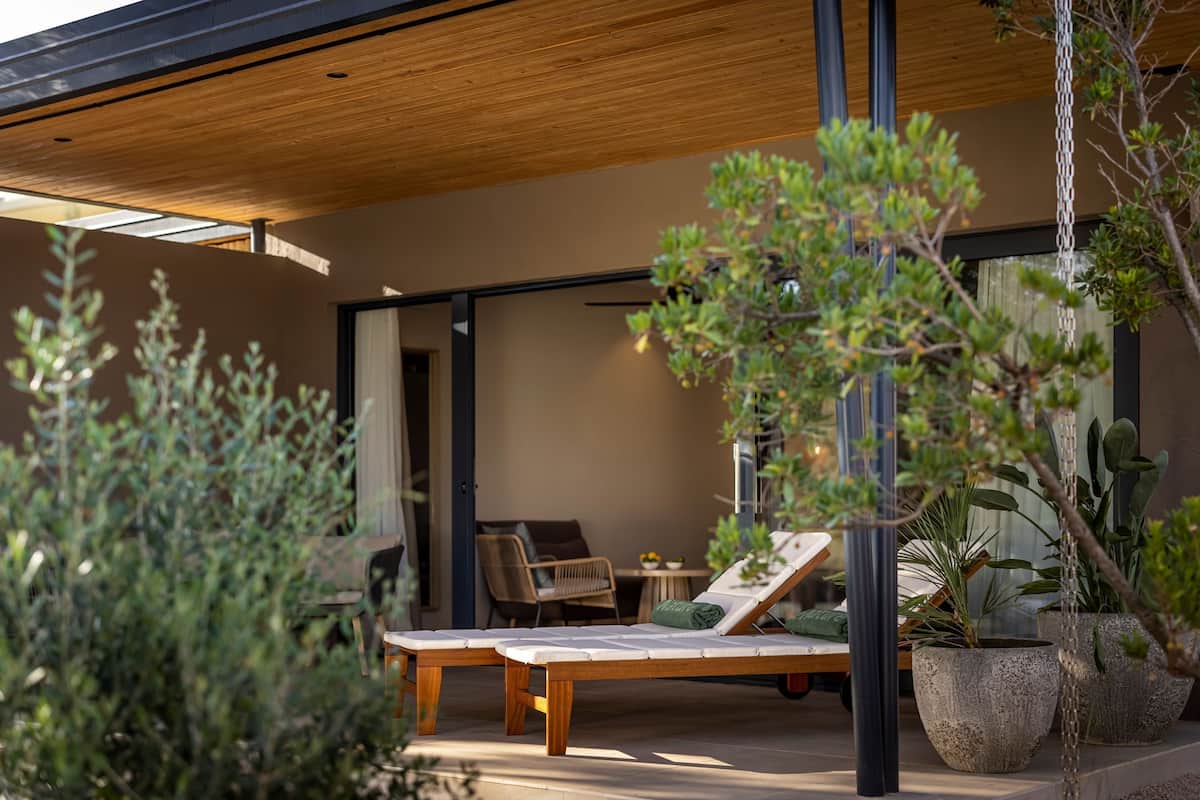 Een moderne buitenlounge met een houten dak, een comfortabele lounge stoel, een bijzettafeltje en potplanten.