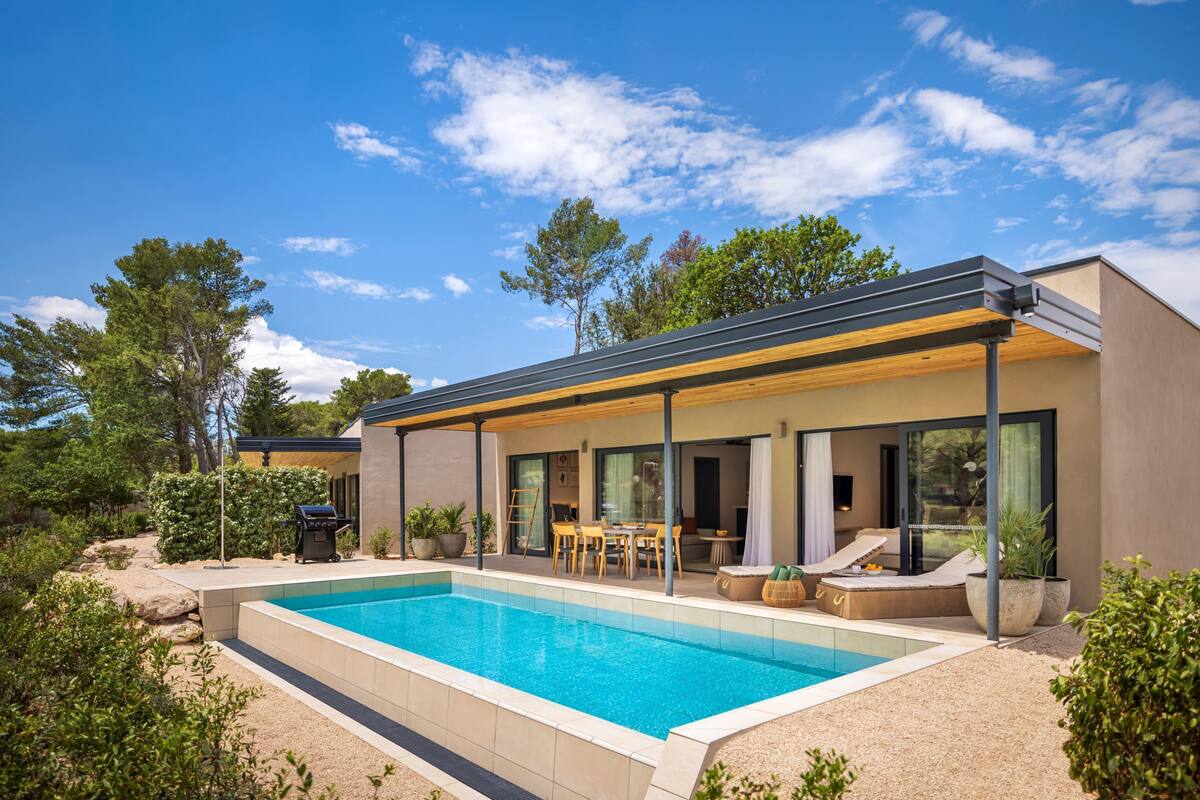 Een modern huis met een zwembad, buitenmeubels en een overdekt terras.