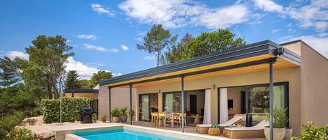 Une maison moderne dotée d’une piscine, d’un espace salon extérieur et d’un patio couvert.