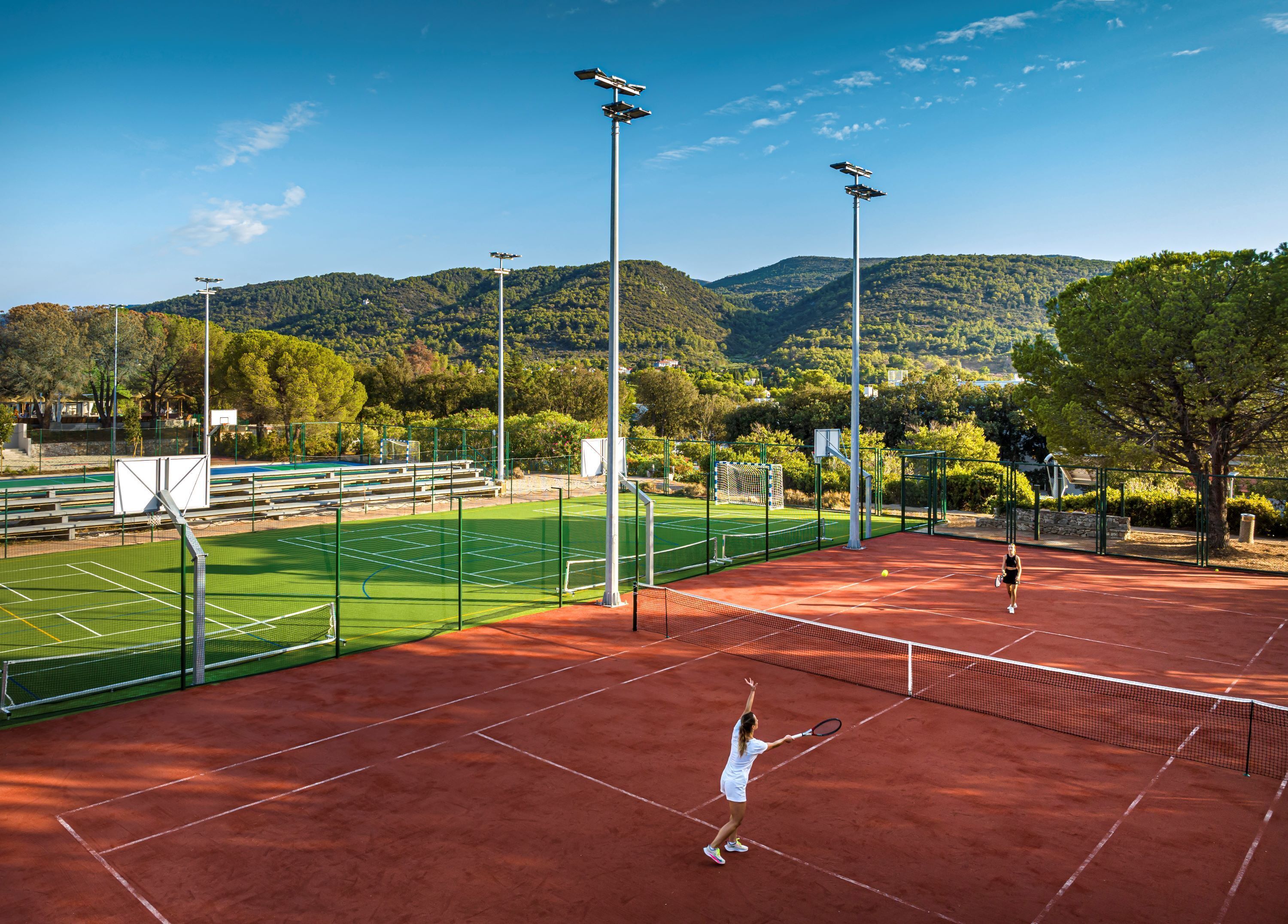Un court de tennis avec un filet, entouré d’une clôture verte et d’arbres.