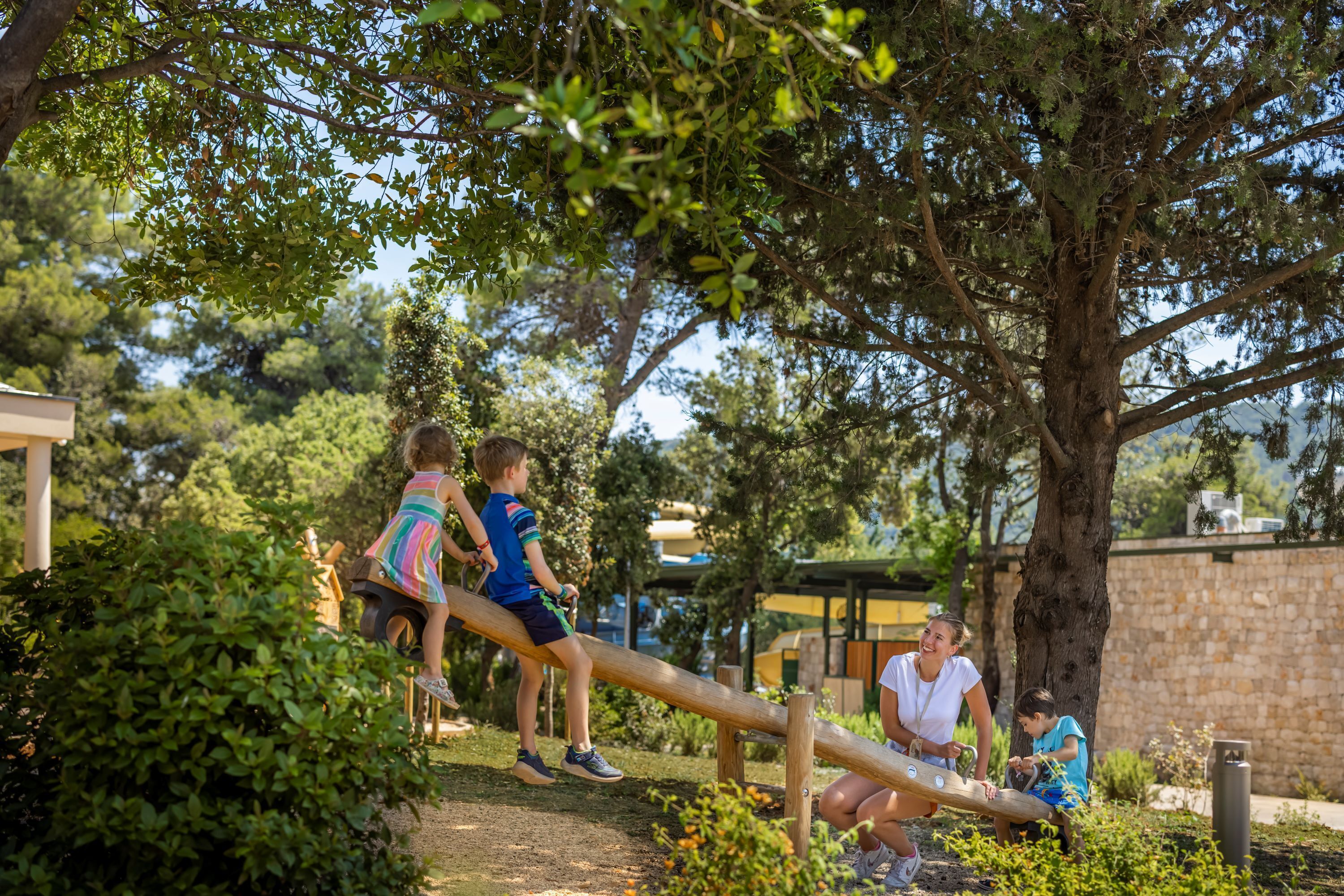 Un parque infantil con un sube y baja y un árbol al fondo.