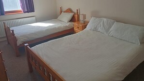 Une chambre avec deux lits simples, une table de chevet en bois avec une lampe et une fenêtre avec des rideaux.