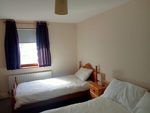 A bedroom with two single beds, a window with curtains, a bedside table with a lamp, and a radiator. - Central 2-bed Apt, Sleeps 5 Above Great Derry Pub (Londonderry)