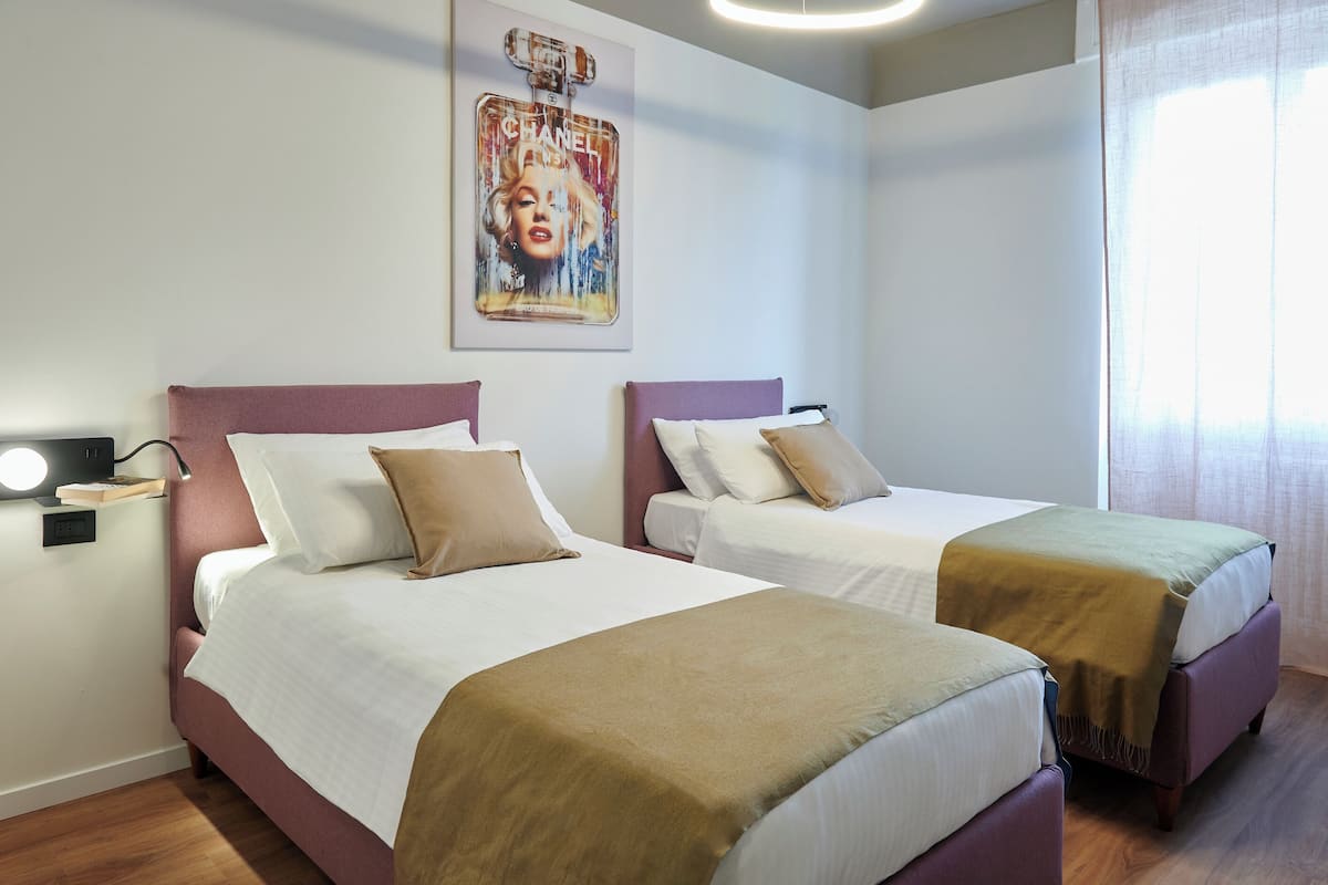 A hotel room with two beds, a nightstand with a lamp, and a wall-mounted artwork.