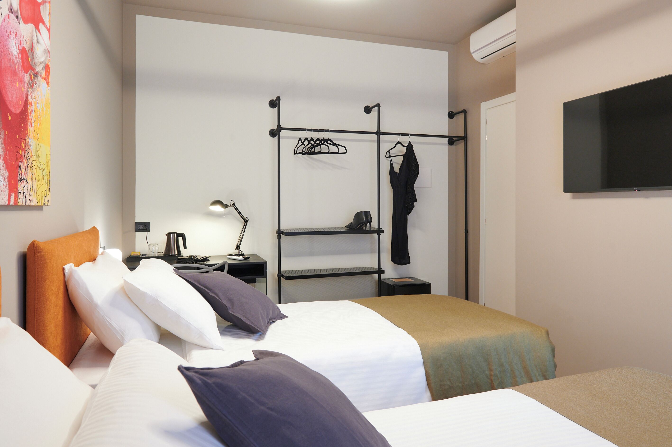 A hotel room with two beds, a TV, a coat rack, and a painting on the wall.
