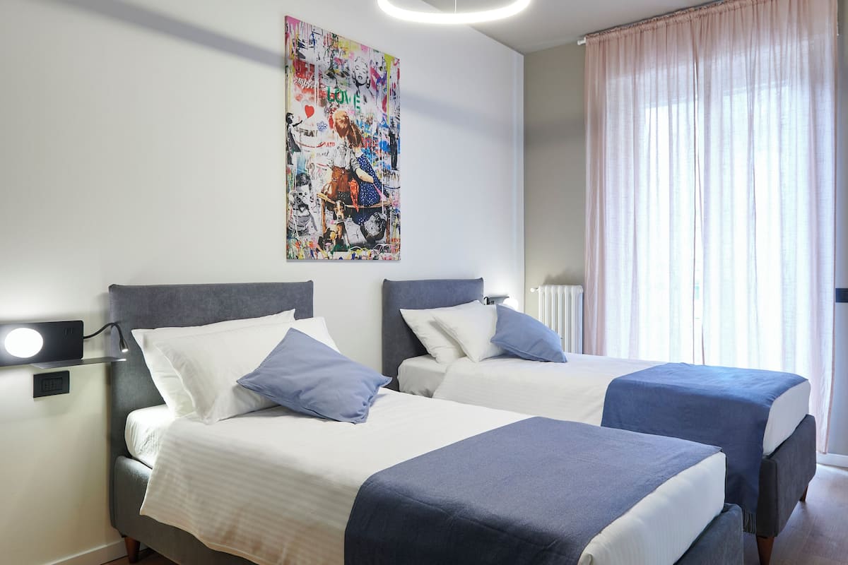 A hotel room with two beds, a wall-mounted artwork, and a window with sheer curtains.