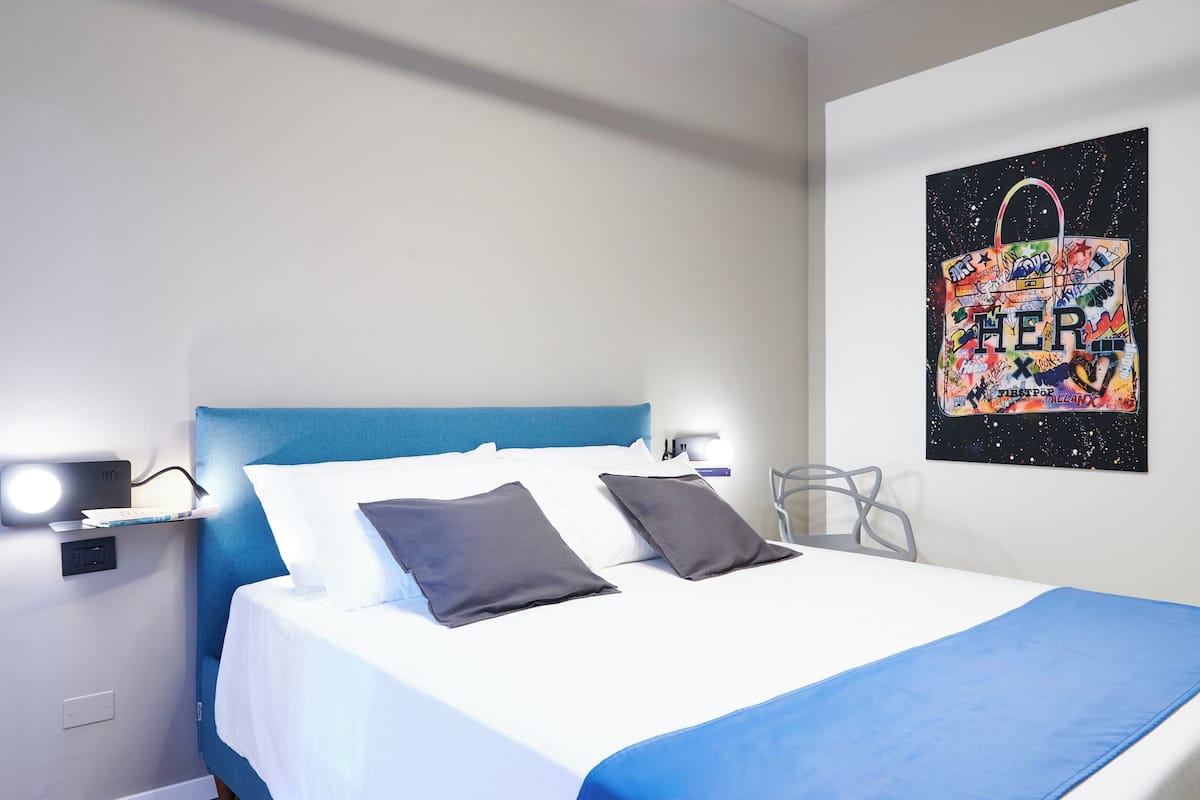 A hotel room with a bed, a desk, and a wall-mounted artwork.