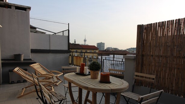 En tagterrasse med træmøbler, et bord og udsigt over by og vand.