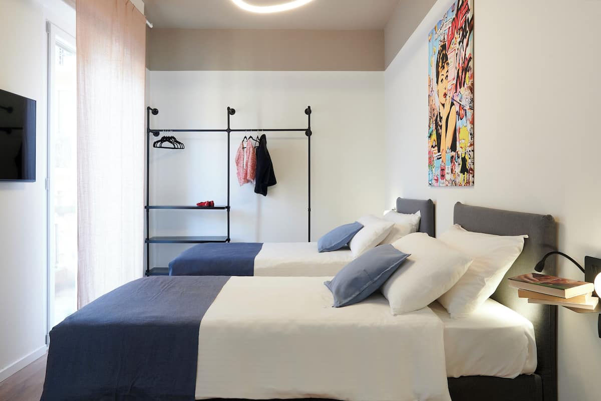 A hotel room with two beds, a wardrobe, a TV, and a painting on the wall.