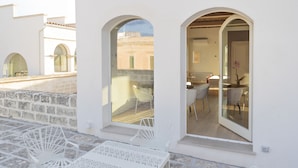 Una terrazza con mobili bianchi, un muro in pietra e vista su un edificio attraverso un arco.