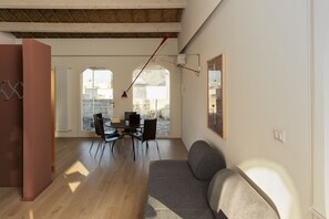 Ein modernes Wohnzimmer mit einer Couch, einem Esstisch und Stühlen. Ein großes Fenster sorgt für natürliches Licht und einen Ausblick ins Freie.