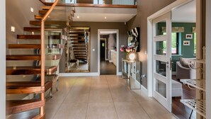 A modern interior with a wooden staircase, a hallway leading to a living area, and a mirrored console table.