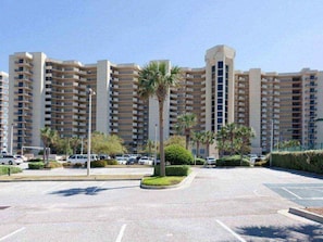 Un hôtel à plusieurs étages, doté d’une tour centrale, d’un parking et de palmiers.