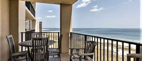 A balcony with a table and chairs, overlooking a beach and ocean.