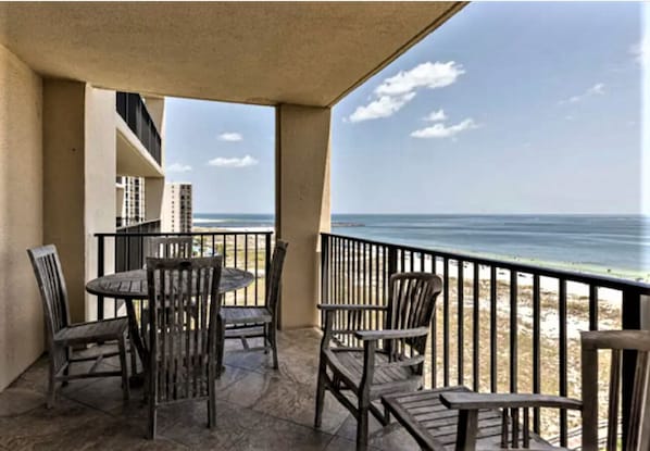 A balcony with a table and chairs, overlooking a beach and ocean.