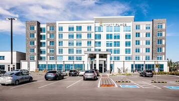 A multi-story hotel with a central entrance, parking lot, and several cars parked in front.