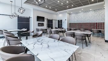 Een moderne congreszaal met marmeren tafels en stoelen, een groot flatscreen televisietoestel en wandpanelen met een geometrisch patroon.