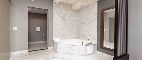 A modern bathroom with a freestanding bathtub, marble walls, and a large mirror.