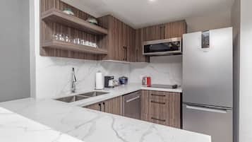 Una cocina moderna con encimeras de mármol, armarios de madera, un refrigerador de acero inoxidable y un microondas integrado.