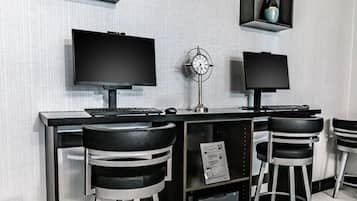 Un espacio de trabajo moderno con dos monitores, un reloj y taburetes altos.