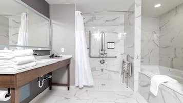 Un baño moderno con suelo de mármol, tocador de madera, espejo grande, bañera y ducha a ras de suelo con puerta de cristal.