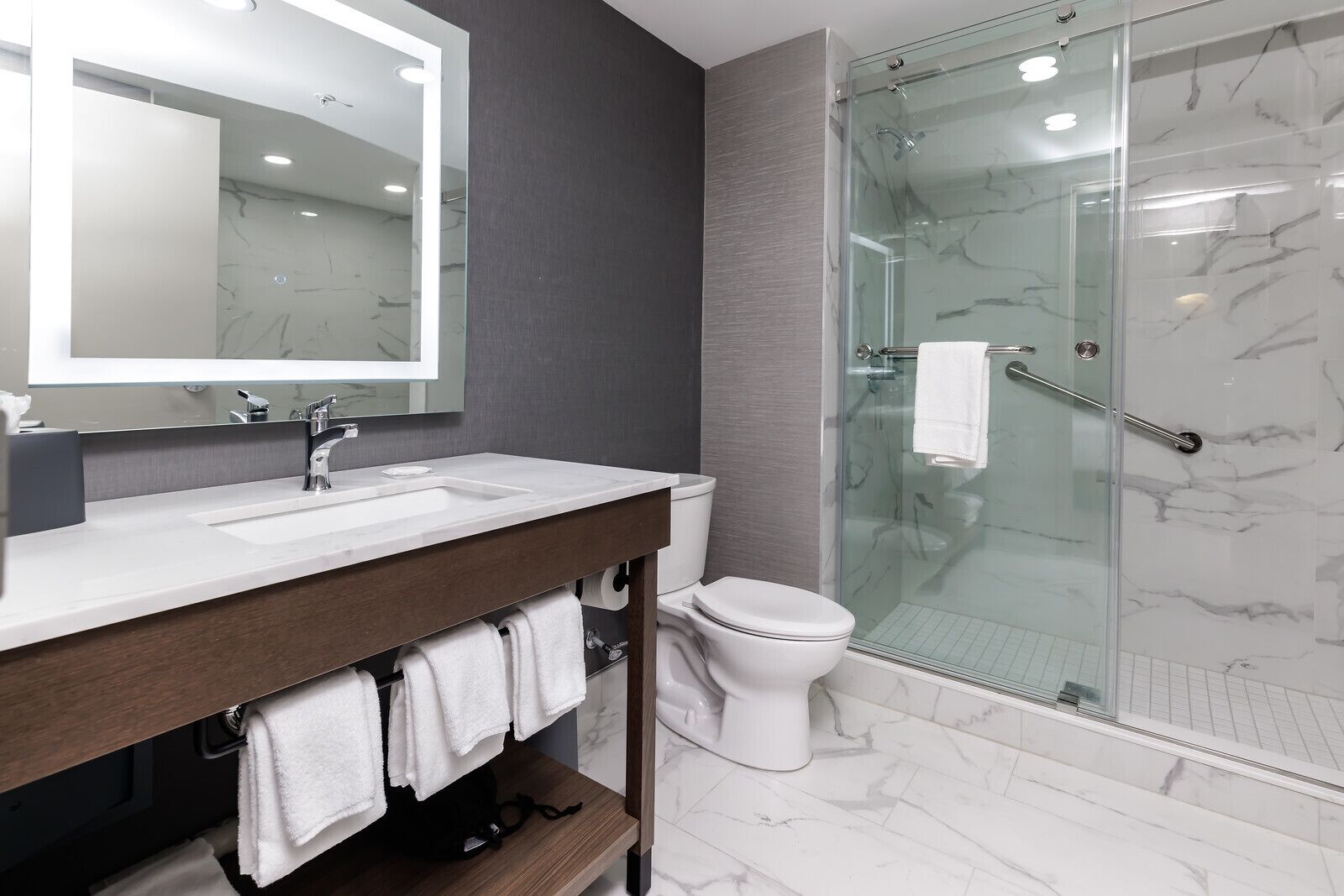 A modern bathroom with a marble-tiled floor, a glass-enclosed shower, a white toilet, and a vanity with a mirror and sink.