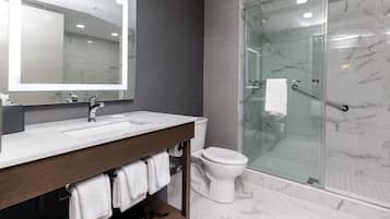 A modern bathroom with a marble-tiled floor, a glass-enclosed shower, a white toilet, and a vanity with a mirror and sink.