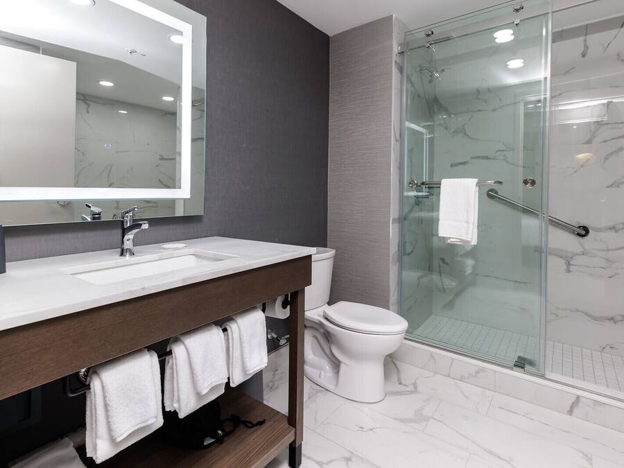 A modern bathroom with a marble-tiled floor, a glass-enclosed shower, a white toilet, and a vanity with a mirror and sink.