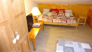 A cozy room with a wooden bed, a television on a wooden table, and a small table with a lamp. - LES MENUIRES apartment sleeps 8 2 bedrooms + mezzanine (LES BELLEVILLE)