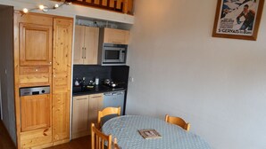 A compact kitchen with wooden cabinets, a microwave, and a small dining table with chairs. - LES MENUIRES apartment sleeps 8 2 bedrooms + mezzanine (LES BELLEVILLE)