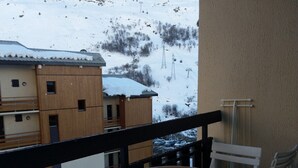 A balcony with a round table and white chairs, overlooking a snowy mountain and buildings. - LES MENUIRES apartment sleeps 8 2 bedrooms + mezzanine (LES BELLEVILLE)