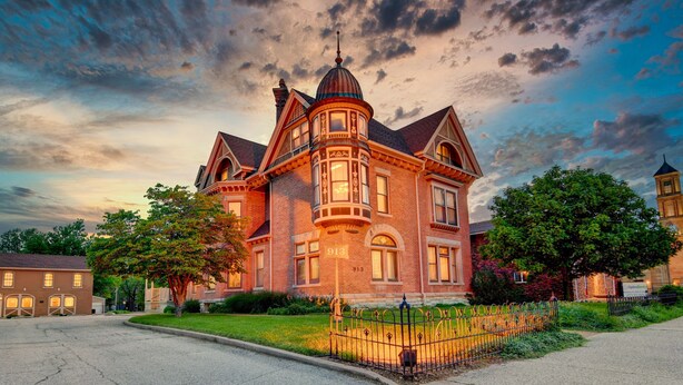 A large, historic brick building with a turret and multiple windows, surrounded by a well-maintained lawn and a metal fence. - Spacious Carriage House | Private Entrance | Historic & Stylish (Springfield)