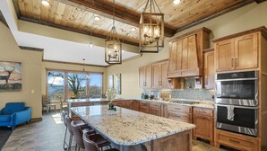 A spacious kitchen with wooden cabinets, a large island with bar stools, and a view of mountains through the windows. - Star Of The Summit, Private Pool, Breathtaking Mountain Views, FREE Tickets! (Sevierville)