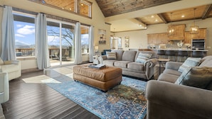 A spacious living room with a large window, a cozy fireplace, and a kitchen area with wooden cabinets. - Star Of The Summit, Private Pool, Breathtaking Mountain Views, FREE Tickets! (Sevierville)