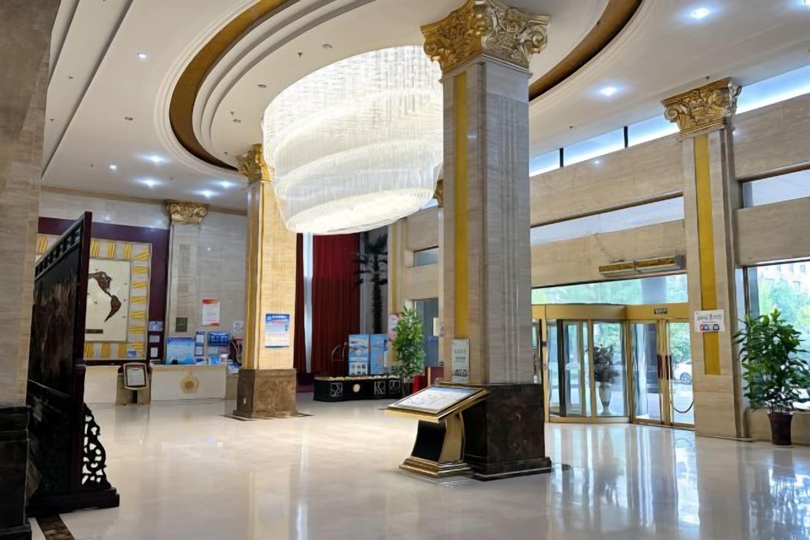 A spacious lobby with a grand chandelier, marble columns, and a reception desk.
