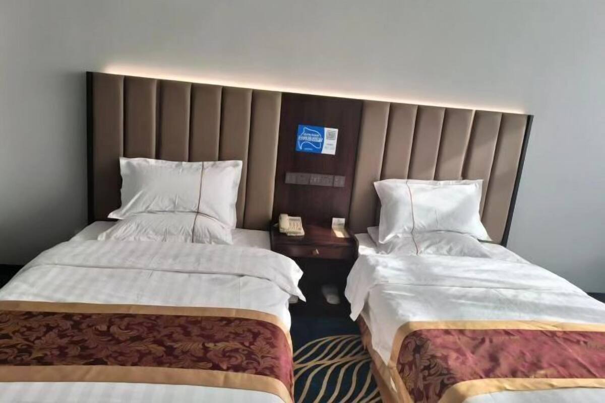 A hotel room with two beds, a headboard with vertical slats, a bedside table with a phone, and a small sign on the wall.