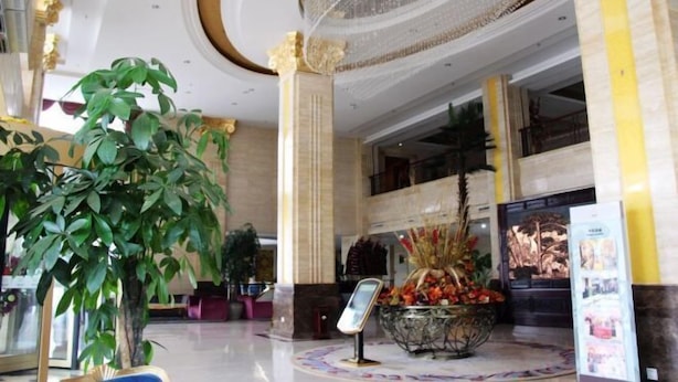 A lobby with a large reception desk, a chandelier, and a decorative plant arrangement.